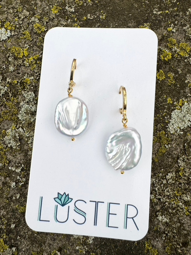 Pair of pearl earrings on a Luster branded card against a textured background
