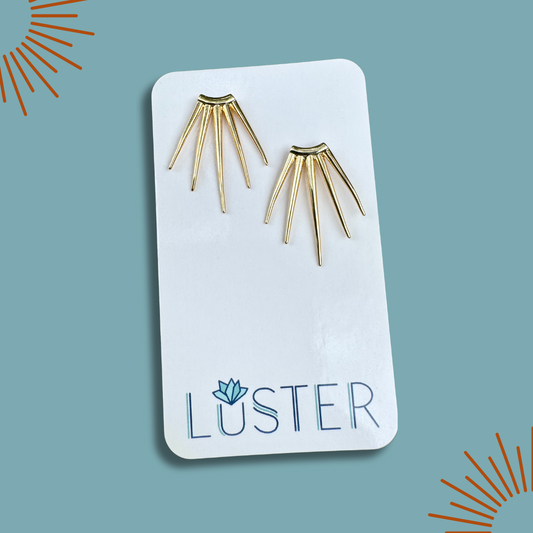 Gold spike earrings on a Luster branded card against a blue background