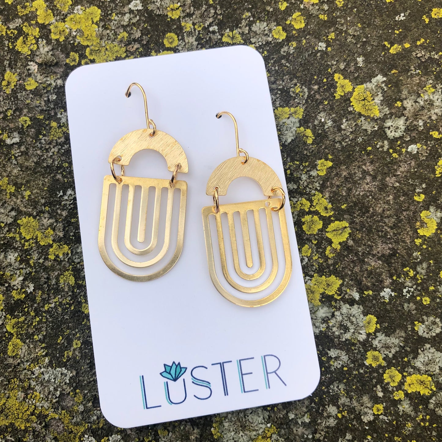 Gold earrings on a Luster branded card against a textured stone background