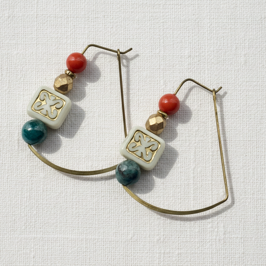 Pair of earrings with square beads and orange and blue accents on a white linen background