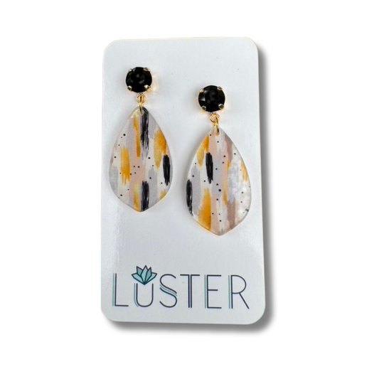 Teardrop-shaped earrings with black and gold accents on a Luster branded card.
