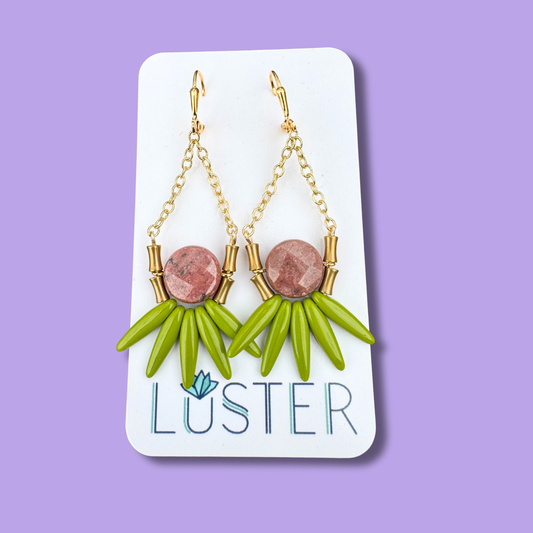 Green earrings with gold accents on a Luster branded card against a purple background