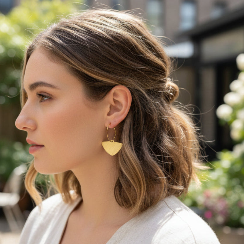 Gold hoop earrings with triangle pendants on a young woman