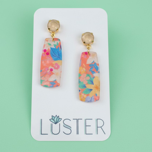 Colorful floral earrings on a Luster branded card against a textured green background