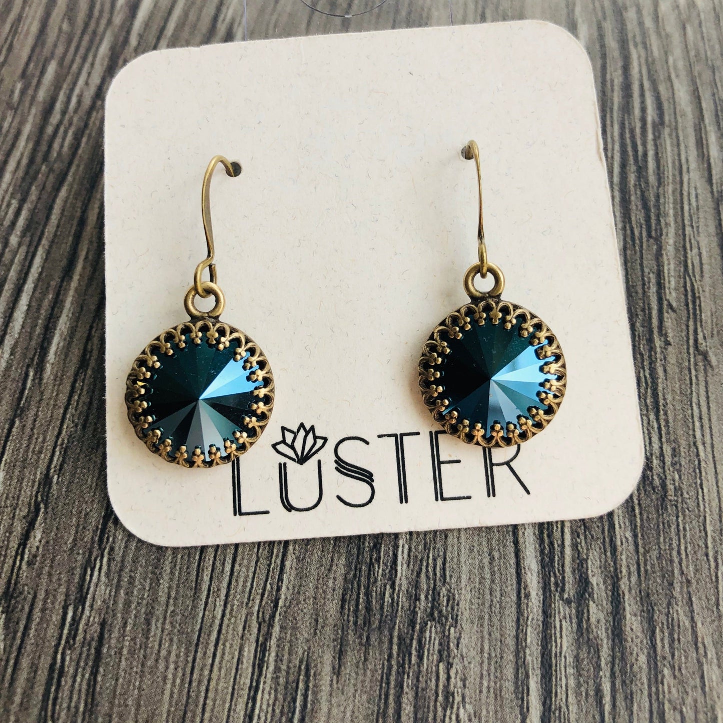 Metallic blue rivoli drop earrings with antique brass-plated bezels, displayed on a card with the brand name 'LUSTER'.