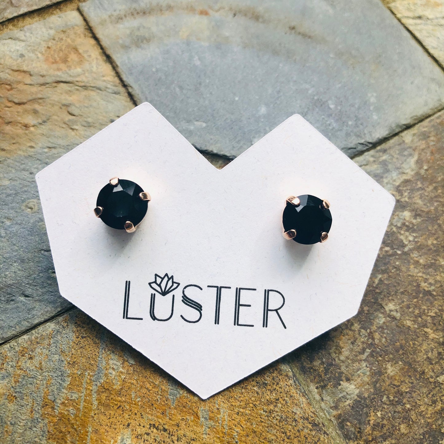 Black stud earrings on a 'Luster' branded card against a stone background