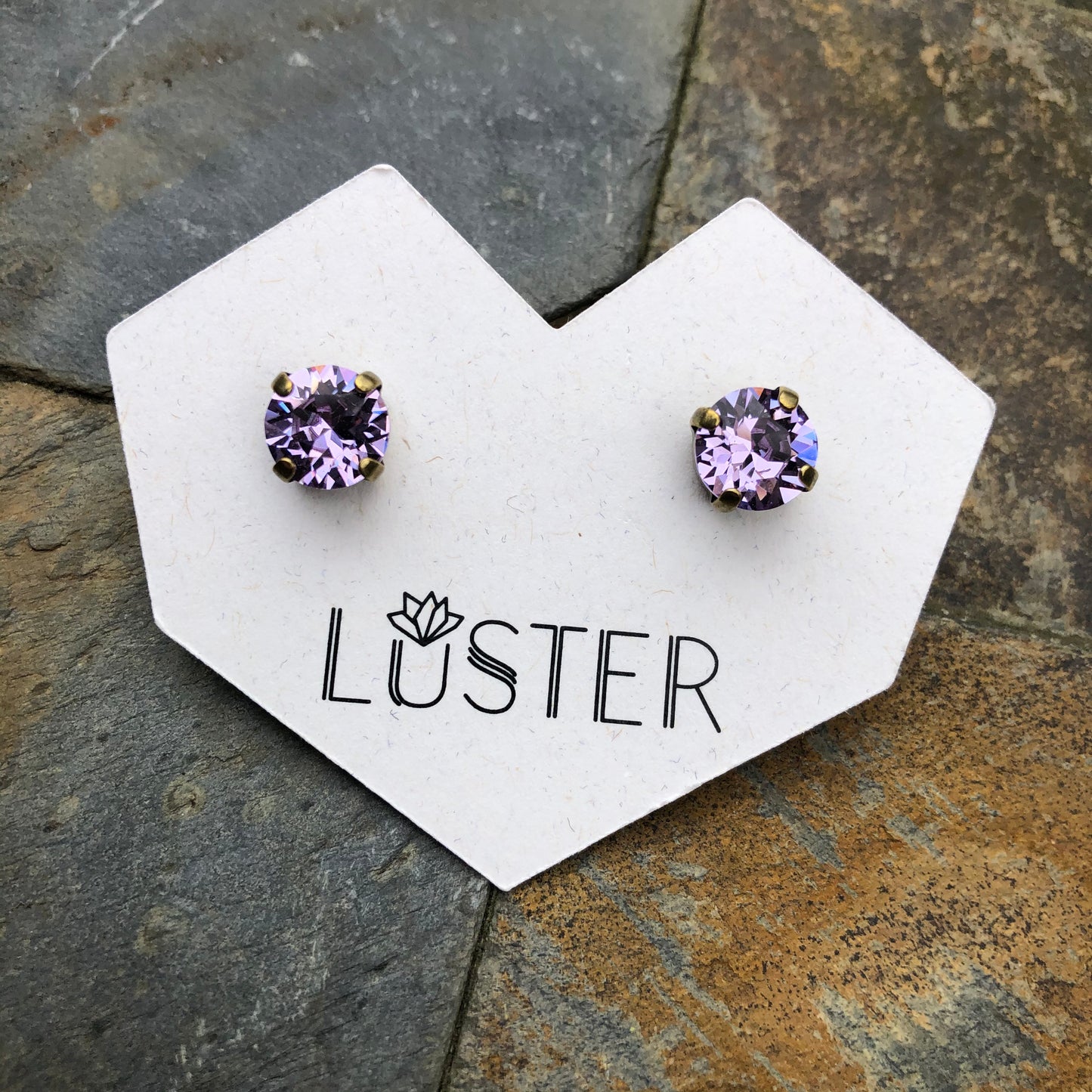 Pair of violet purple gemstone earrings on a Luster branded card against a stone background