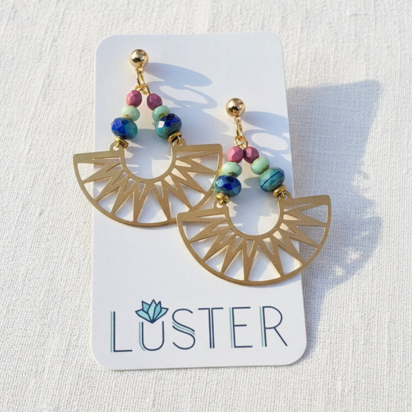 Gold earrings with colorful beads on a Luster branded card against a white linen background