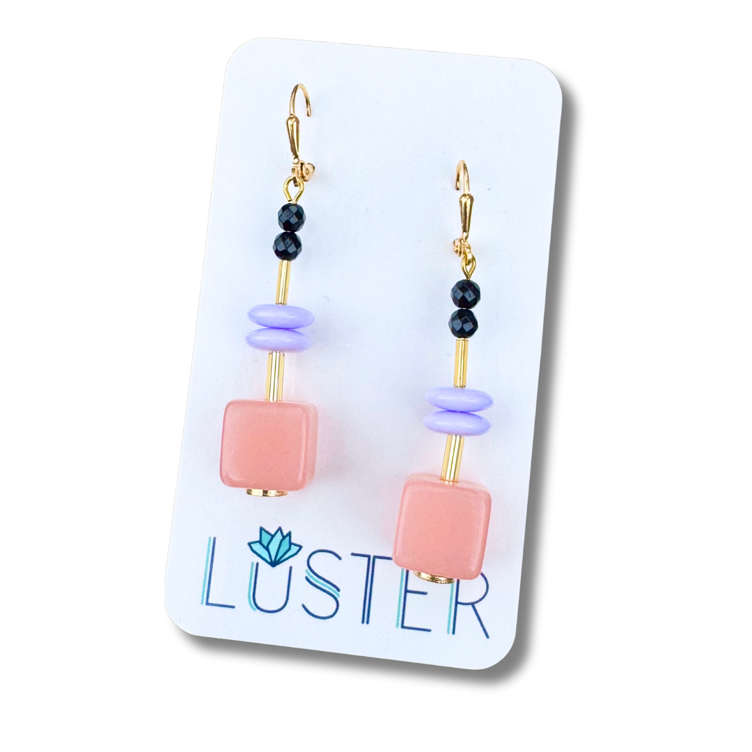 Pair of earrings on a Luster branded card with pink, purple, and black beads.
