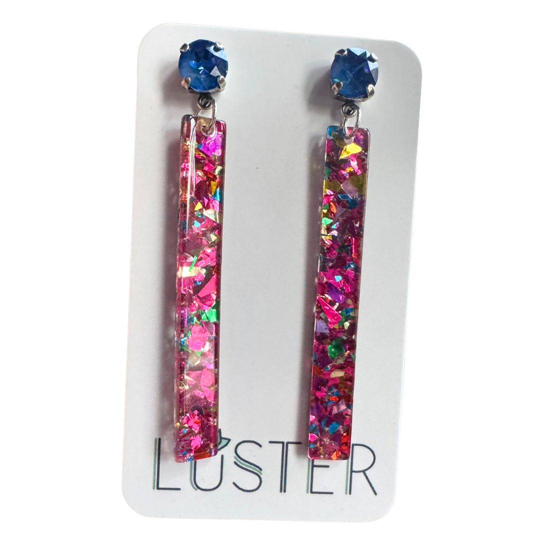 Multicolored glittery earrings on a white card with 'Luster' branding.