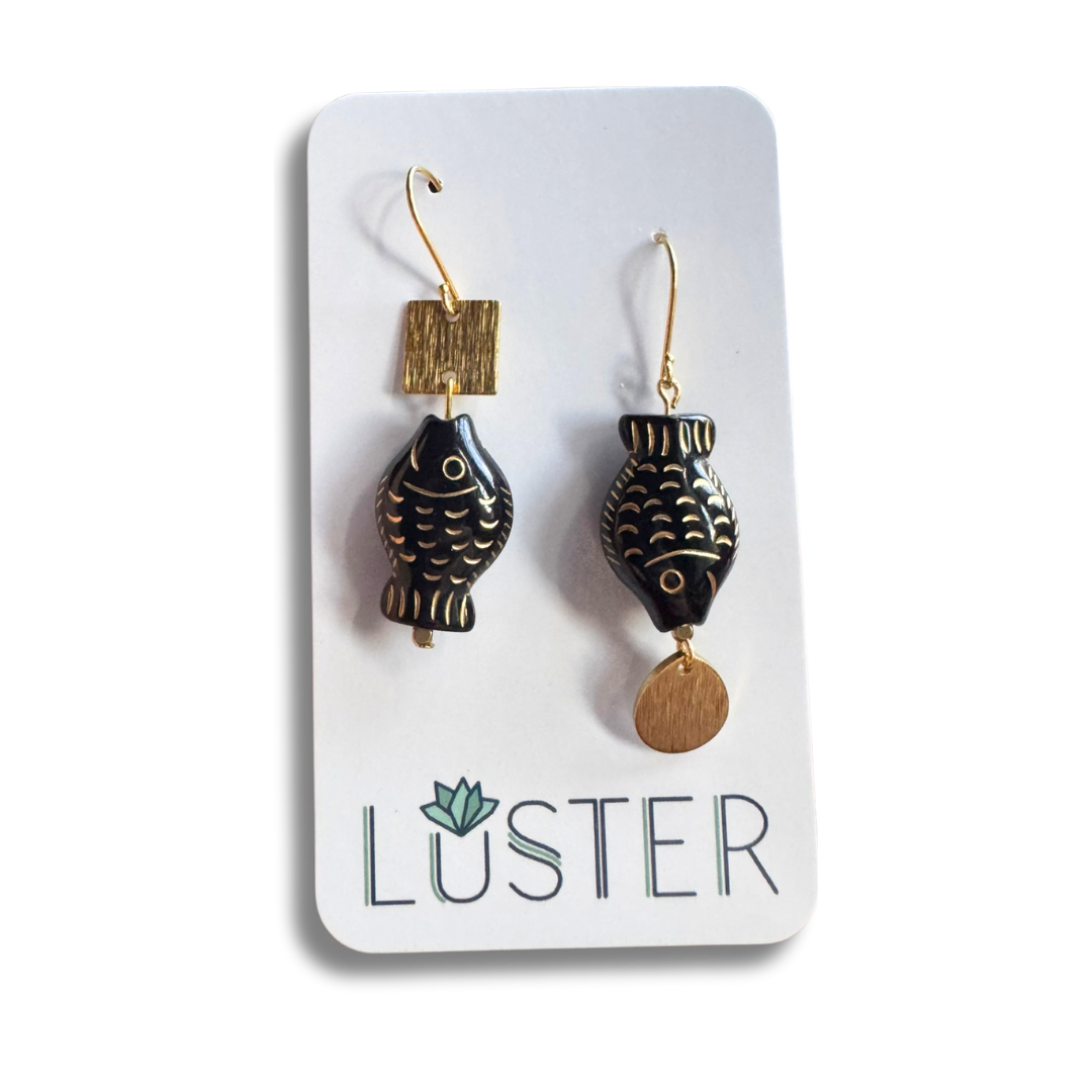 Black and gold fish-shaped earrings on a Luster branded card.