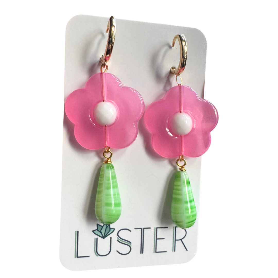 Pink flower-shaped earrings with green teardrop charms on a Luster branded card.