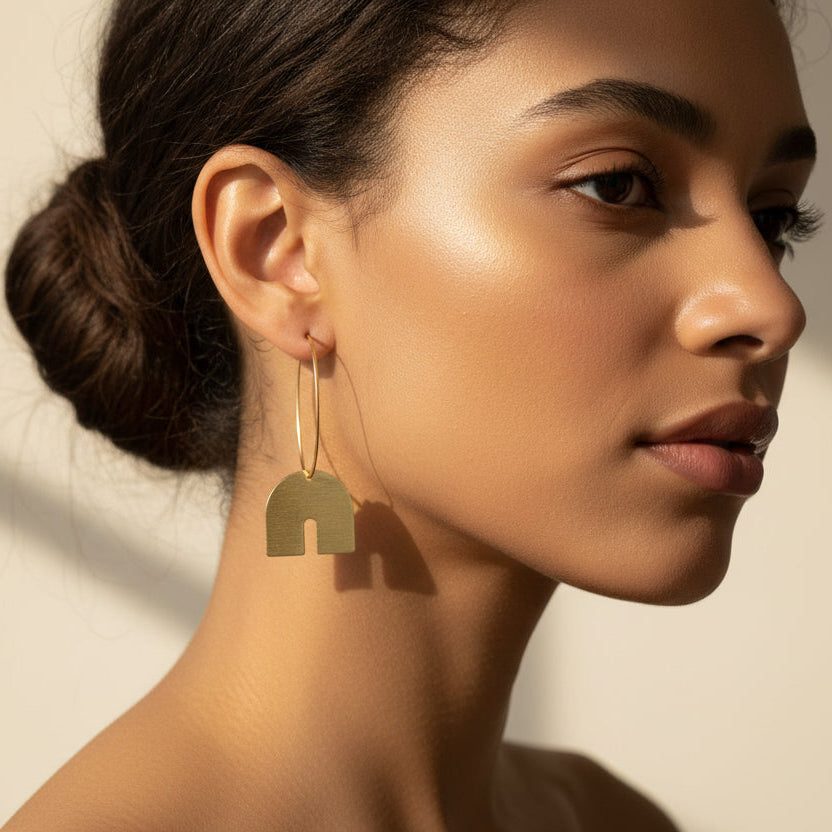 Pair of gold hoop earrings with arch-shaped pendants on a woman