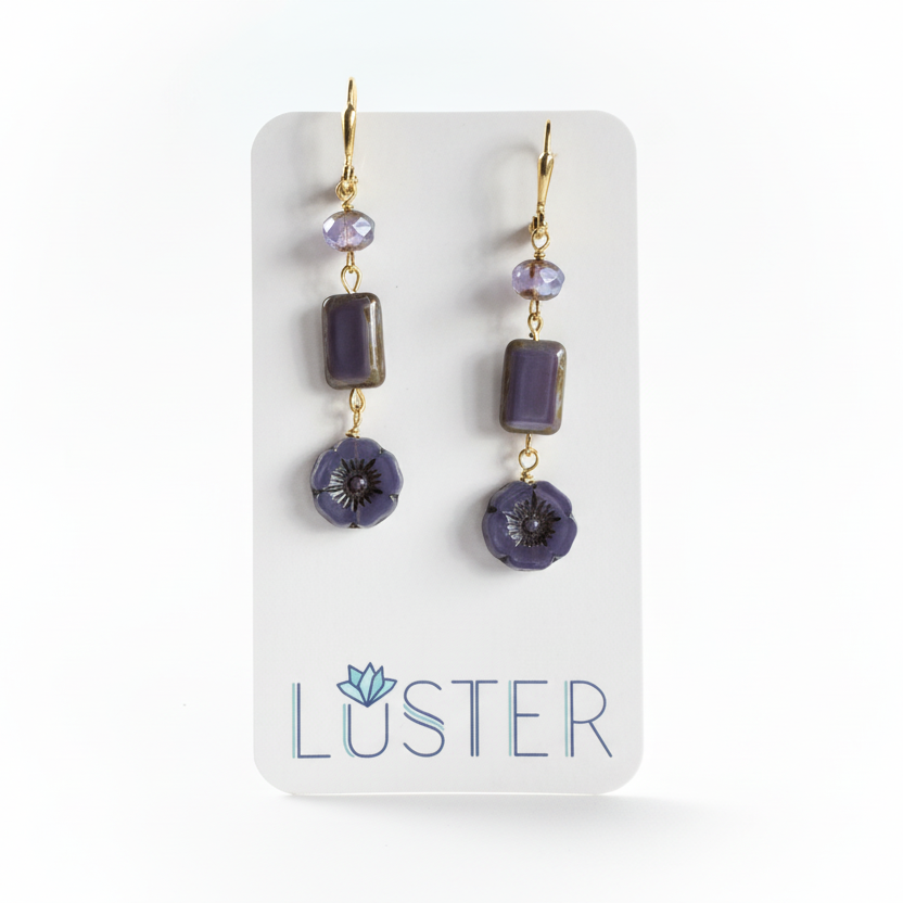 Pair of purple beaded earrings on a Luster branded card.