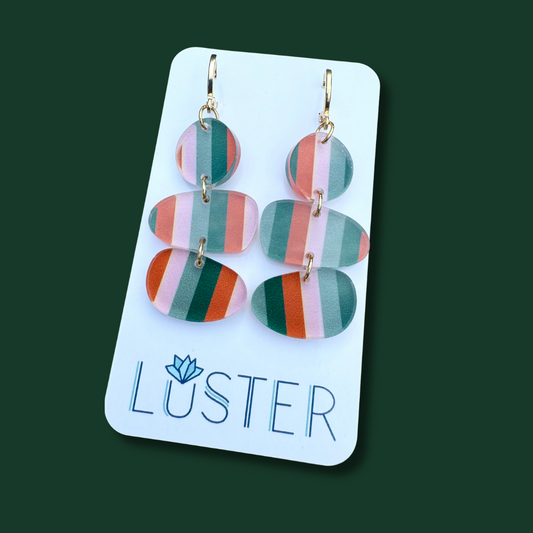 Colorful striped earrings on a Luster branded card against a dark green background