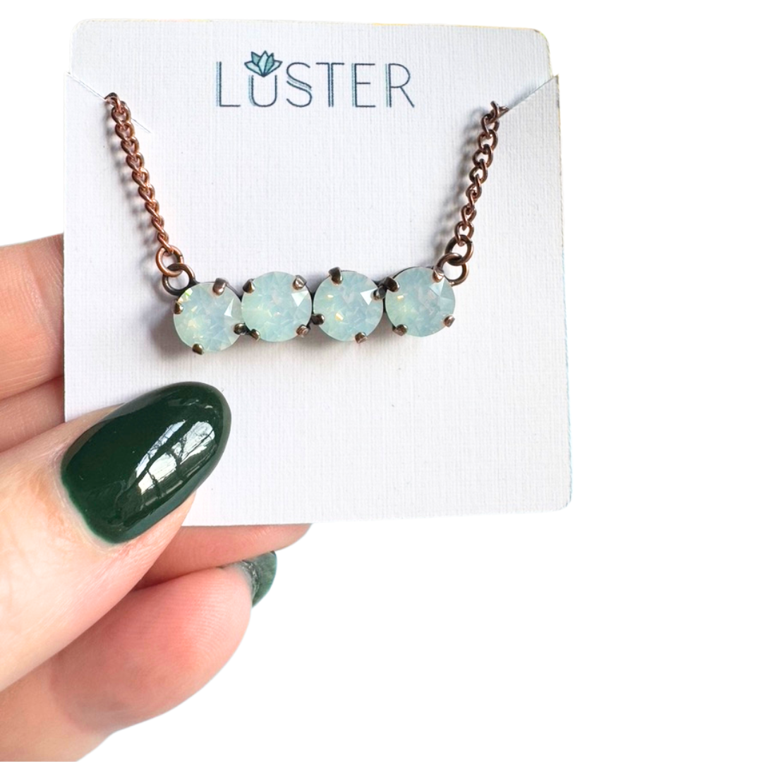 Necklace with milky white crystals on a 'Luster' branded card held by a hand with green nail polish.
