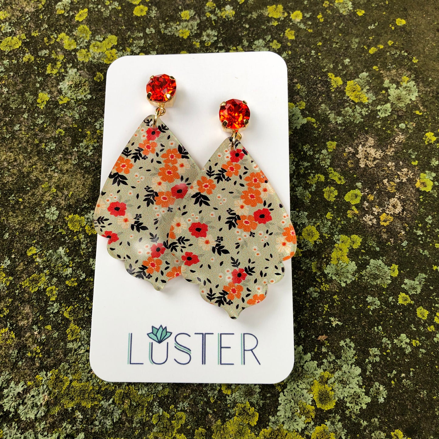 A pair of sage green floral teardrop earrings with hyacinth crystal accents displayed on a card with the brand name LUSTER.