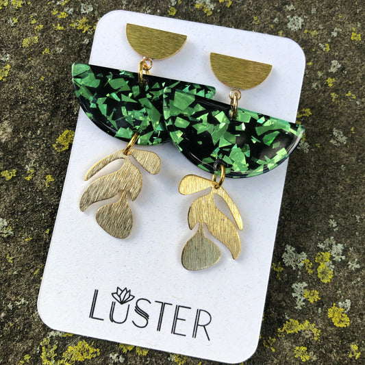 A pair of emerald green confetti-shaped earrings with gold brass accents, displayed on a white card with the brand name 'LUSTER'.