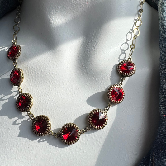A siam red Swarovski rivoli link necklace with an adjustable antique brass chain and lobster clasp, displayed on a mannequin.