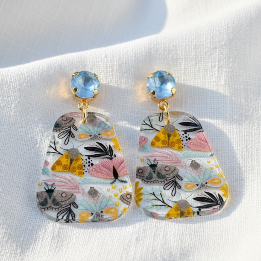 Pair of floral earrings with colorful stones on a white fabric background
