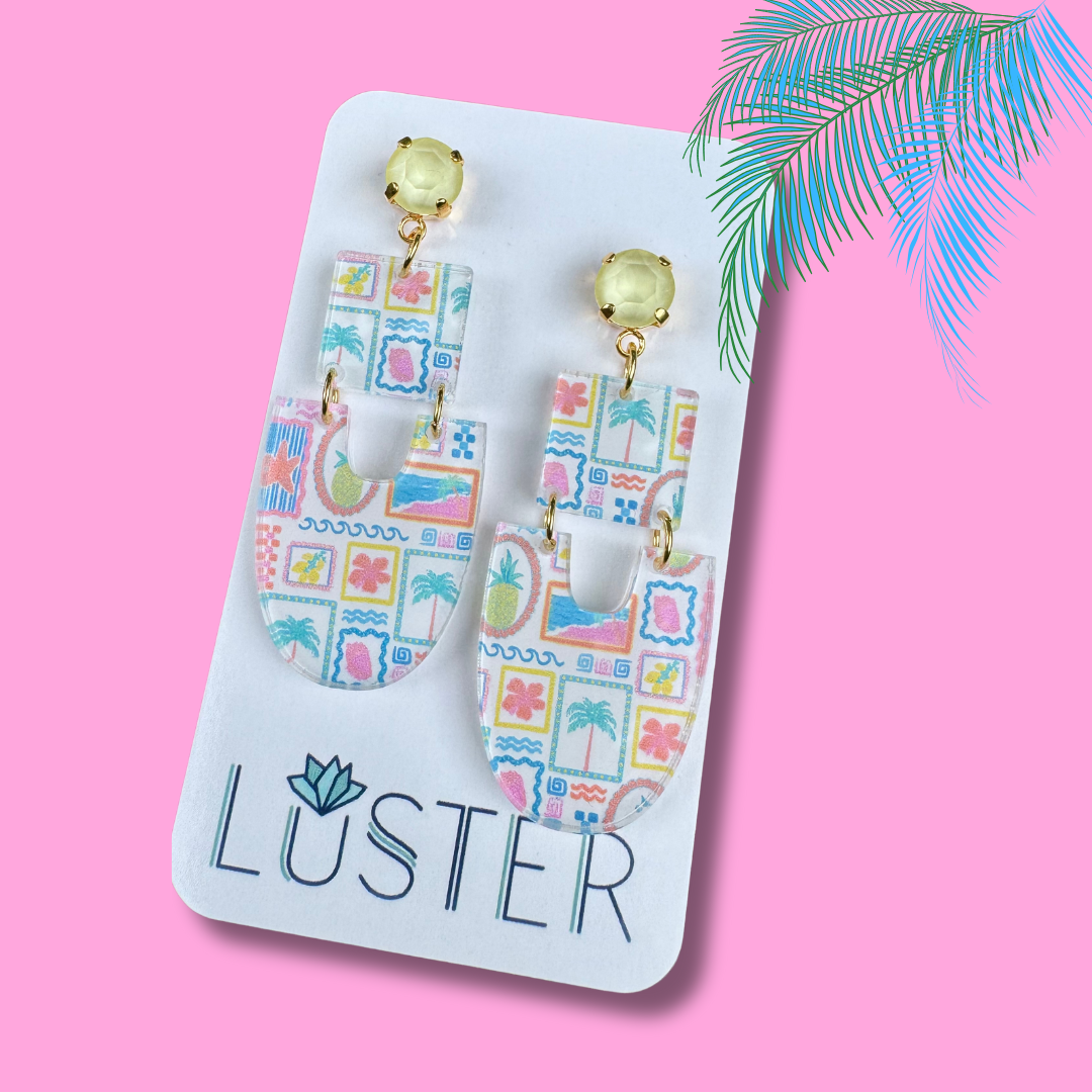 Tropical-themed earrings on a Luster branded card against a pink background with palm leaves.