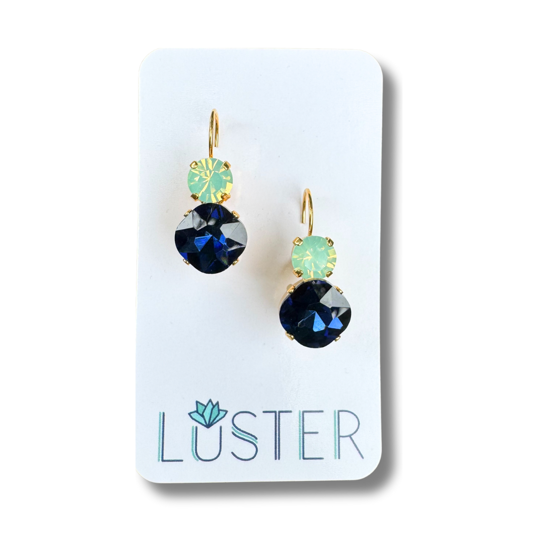 Pair of earrings with blue and green crystals on a Luster branded card.