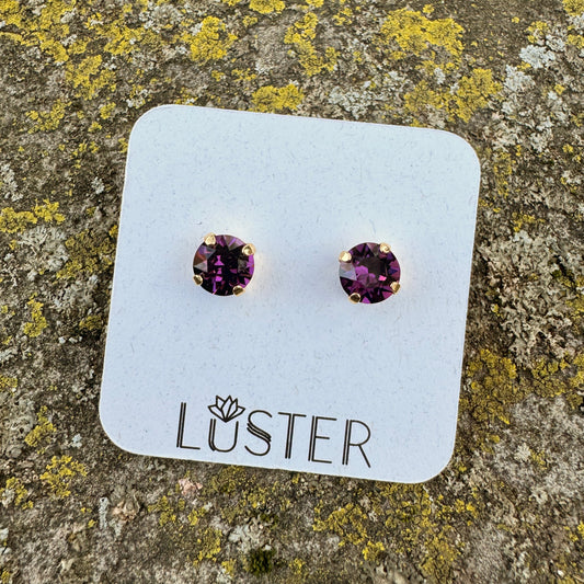 Purple round stud earrings on a Luster branded card against a textured stone background