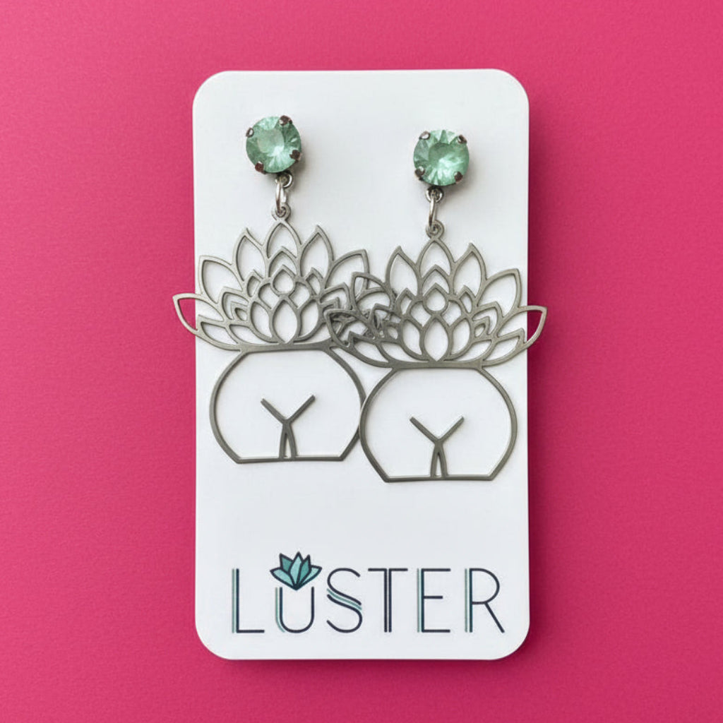 Luster earrings on a card with green gemstones against a pink background
