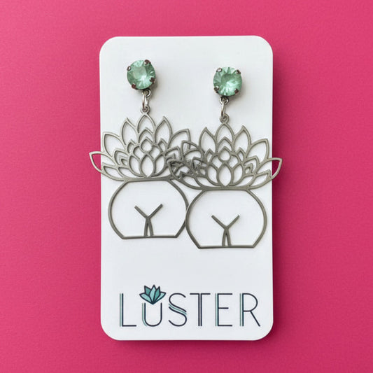 Luster earrings on a card with green gemstones against a pink background