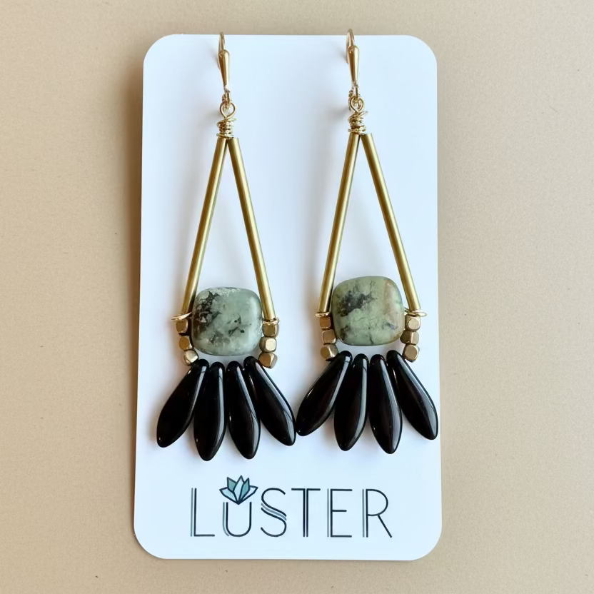 Green stones with black thorn accents on brass leverbacks on Luster branded card against a leafy background.