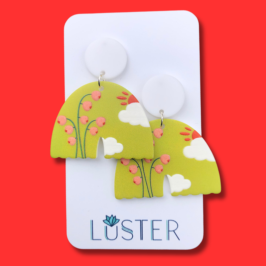 Pair of green earrings with floral design on a Luster branded card against a red background