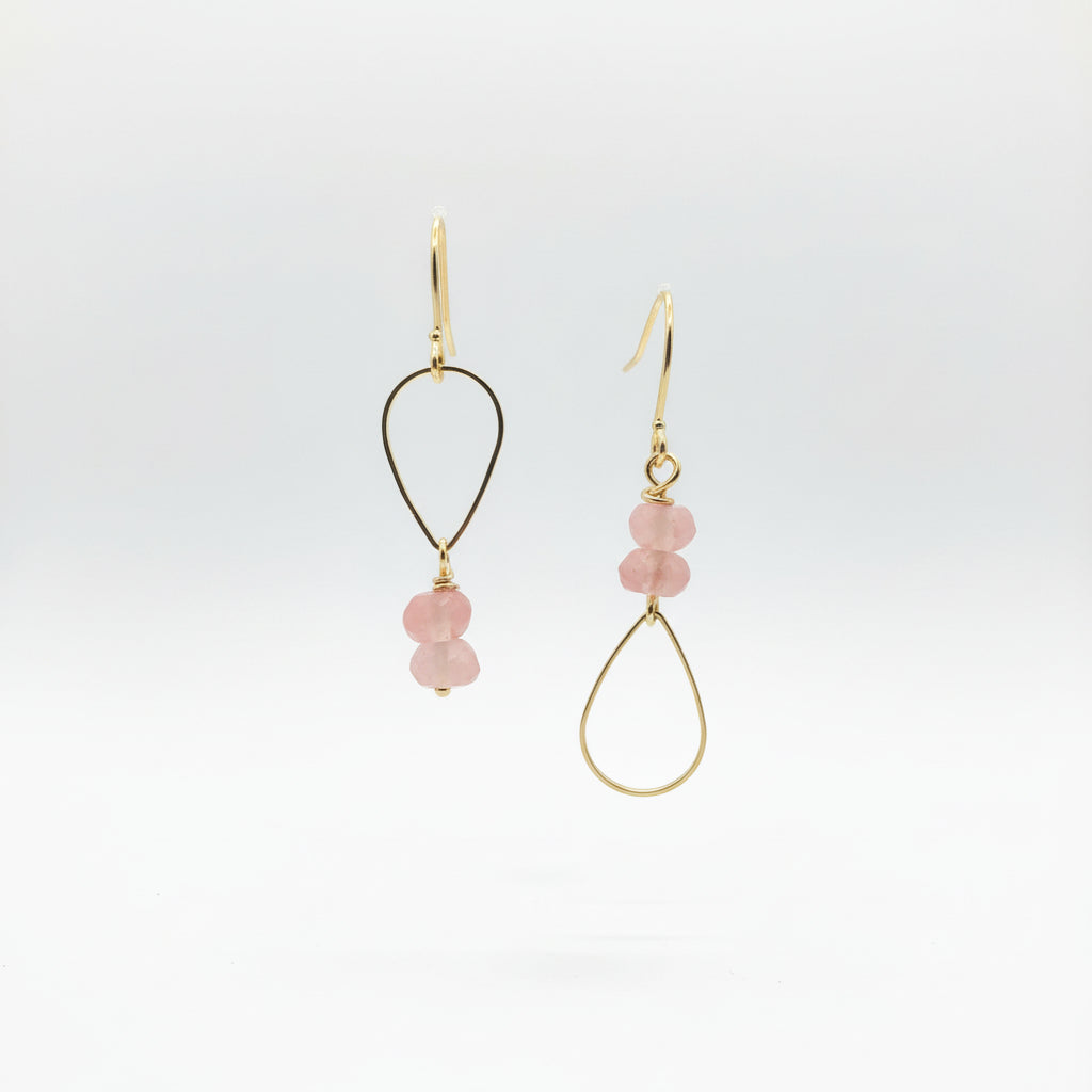 Gold earrings with pink beads on a Luster branded card against a natural background