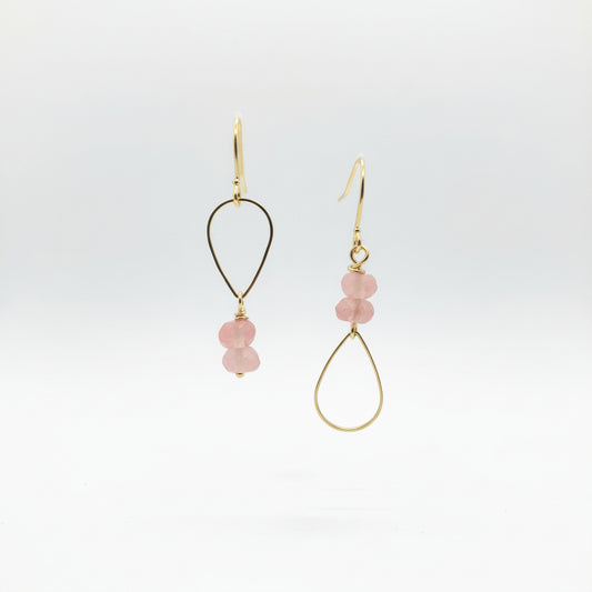 Gold earrings with pink beads on a Luster branded card against a natural background