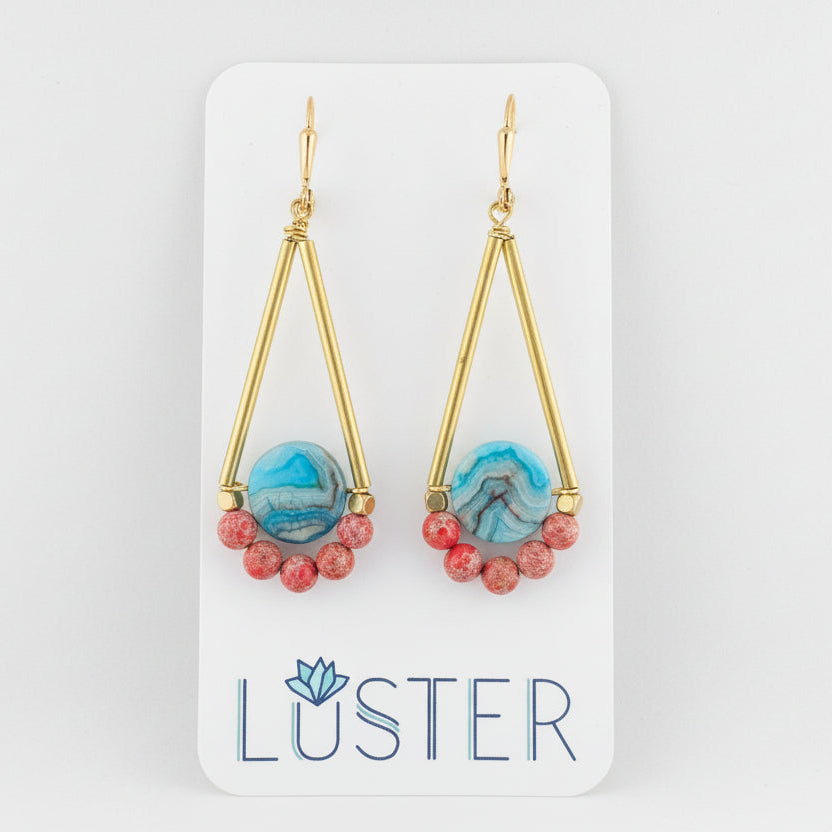 A pair of gold brass earrings with streaked teal crazy lace agate coins and red-orange impression jasper beads, displayed on a card with the brand name LUSTER.