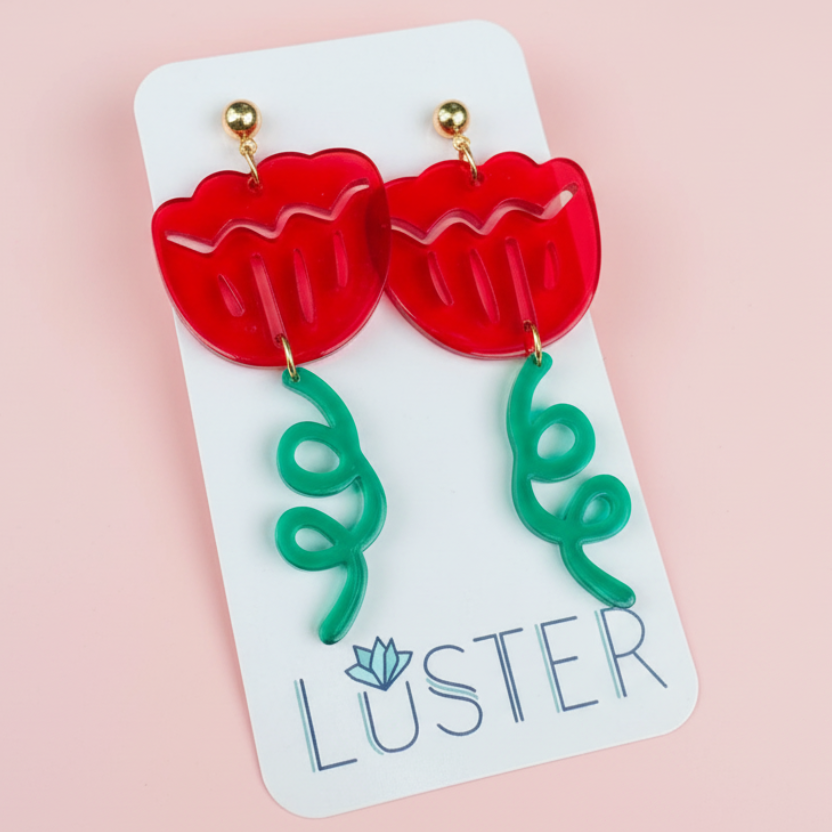 Red flower-shaped earrings on a Luster branded card against a pink background