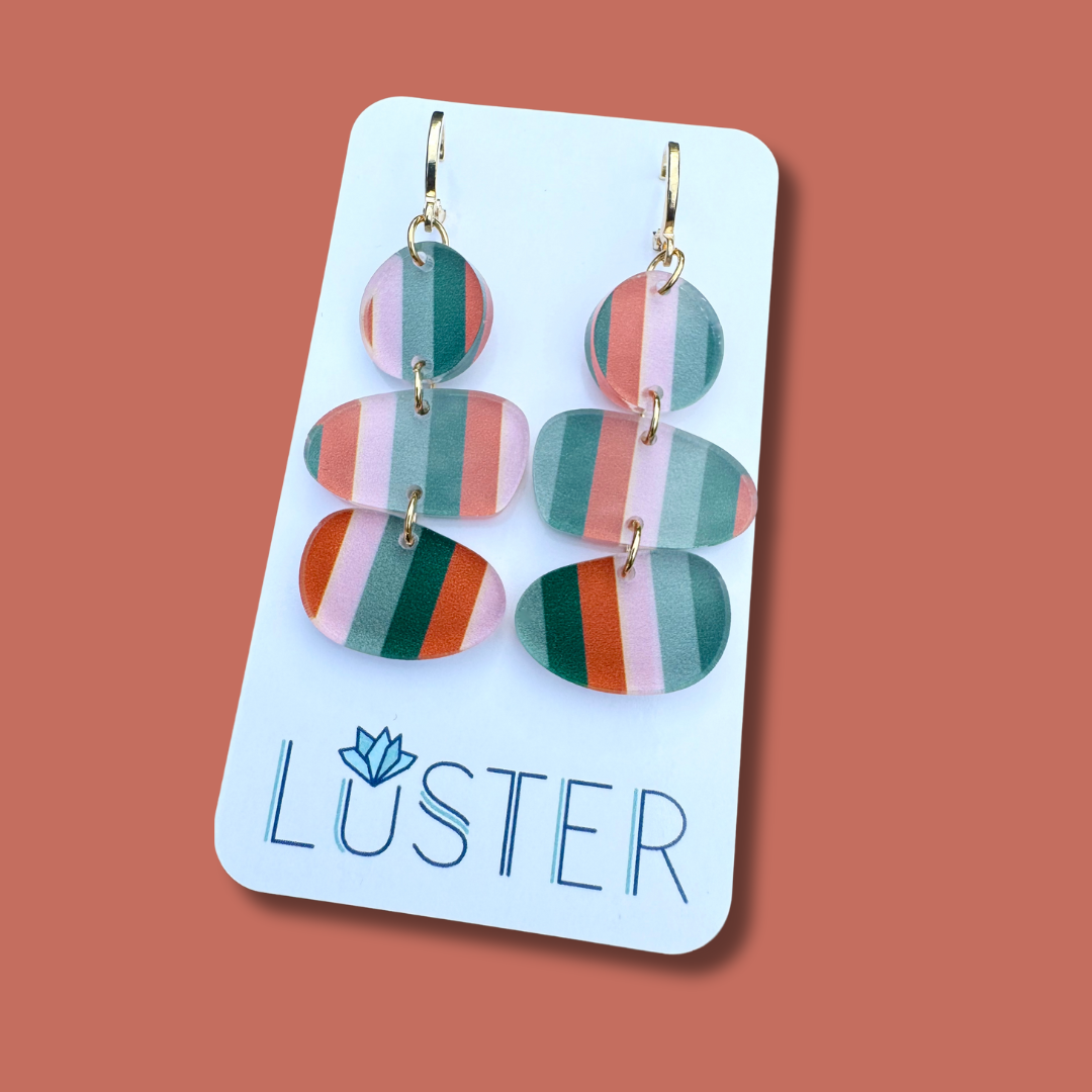 Colorful striped earrings on a Luster branded card against a brown background