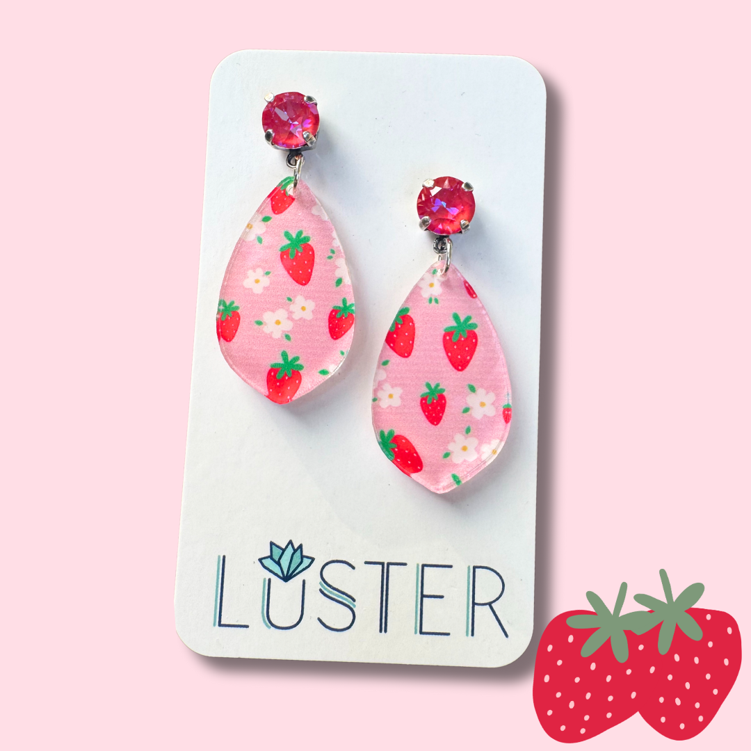 Teardrop-shaped earrings with strawberry pattern on a 'Luster' branded card against a pink background.
