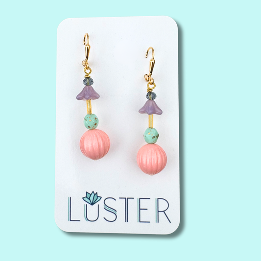 Pair of pink round dangle earrings on a Luster branded card against a light blue background