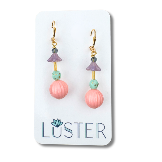 Pair of earrings with pink and green beads on a Luster branded card.