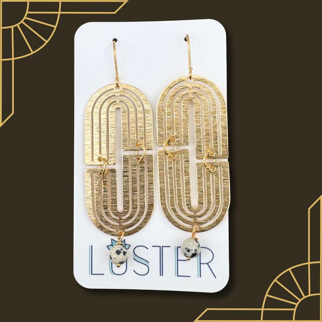 Gold earrings with stone drops on a Luster branded card against a dark background