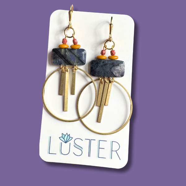 Pair of brass and stone earrings on a Luster branded card against a purple background