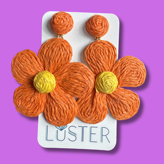 Orange flower-shaped earrings on a Luster branded card against a purple background