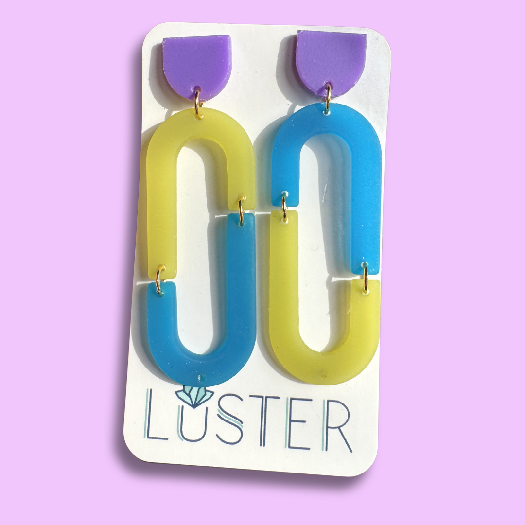 Colorful loop-shaped earrings on a Luster branded card against a purple background