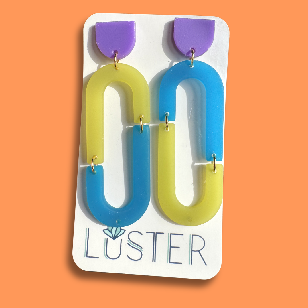 Colorful loop-shaped earrings on a Luster branded card against an orange background