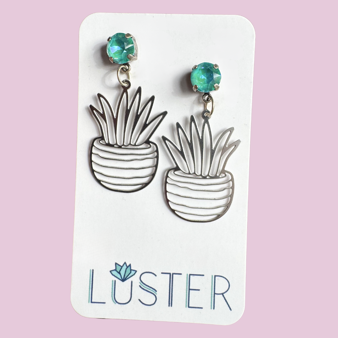 Pendant earrings with plant design on a Luster branded card against a pink background