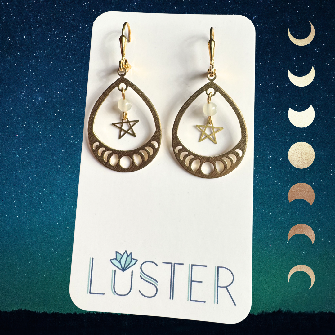 Gold teardrop earrings with star and moon phases on a Luster branded card against a starry night sky background.