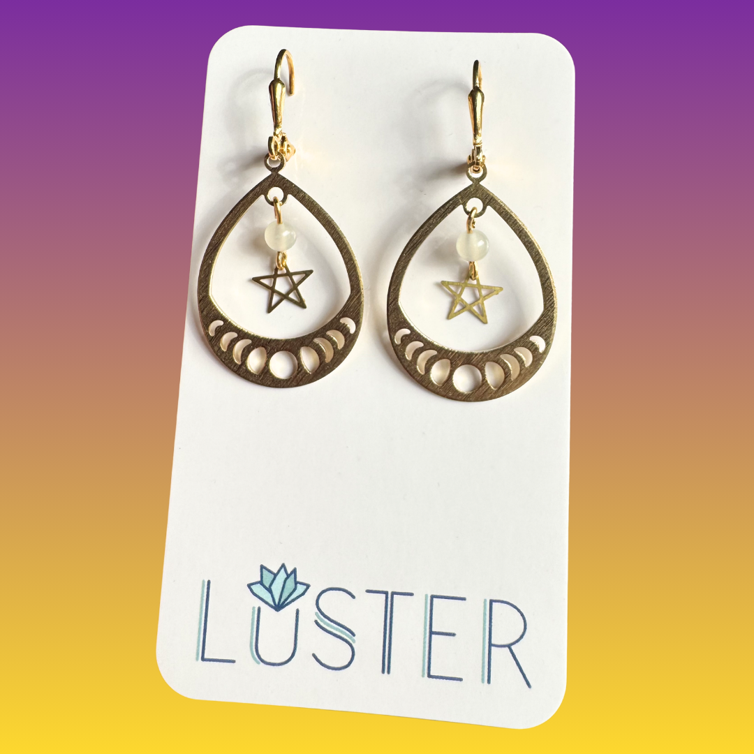 Gold teardrop earrings with star and moon designs on a Luster branded card against a gradient background.
