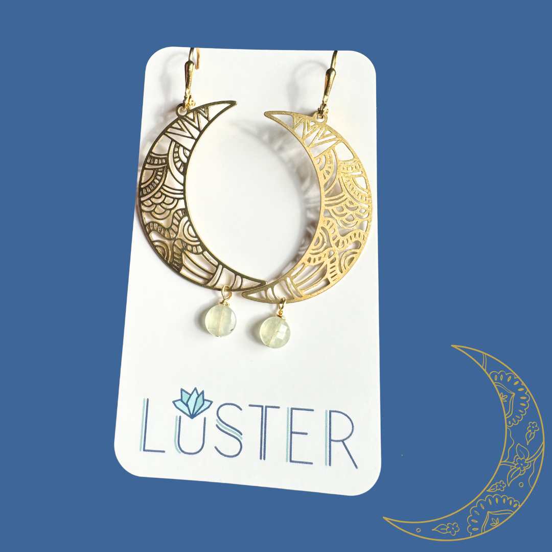 Gold crescent moon earrings with dangling beads on a Luster branded card against a blue background.