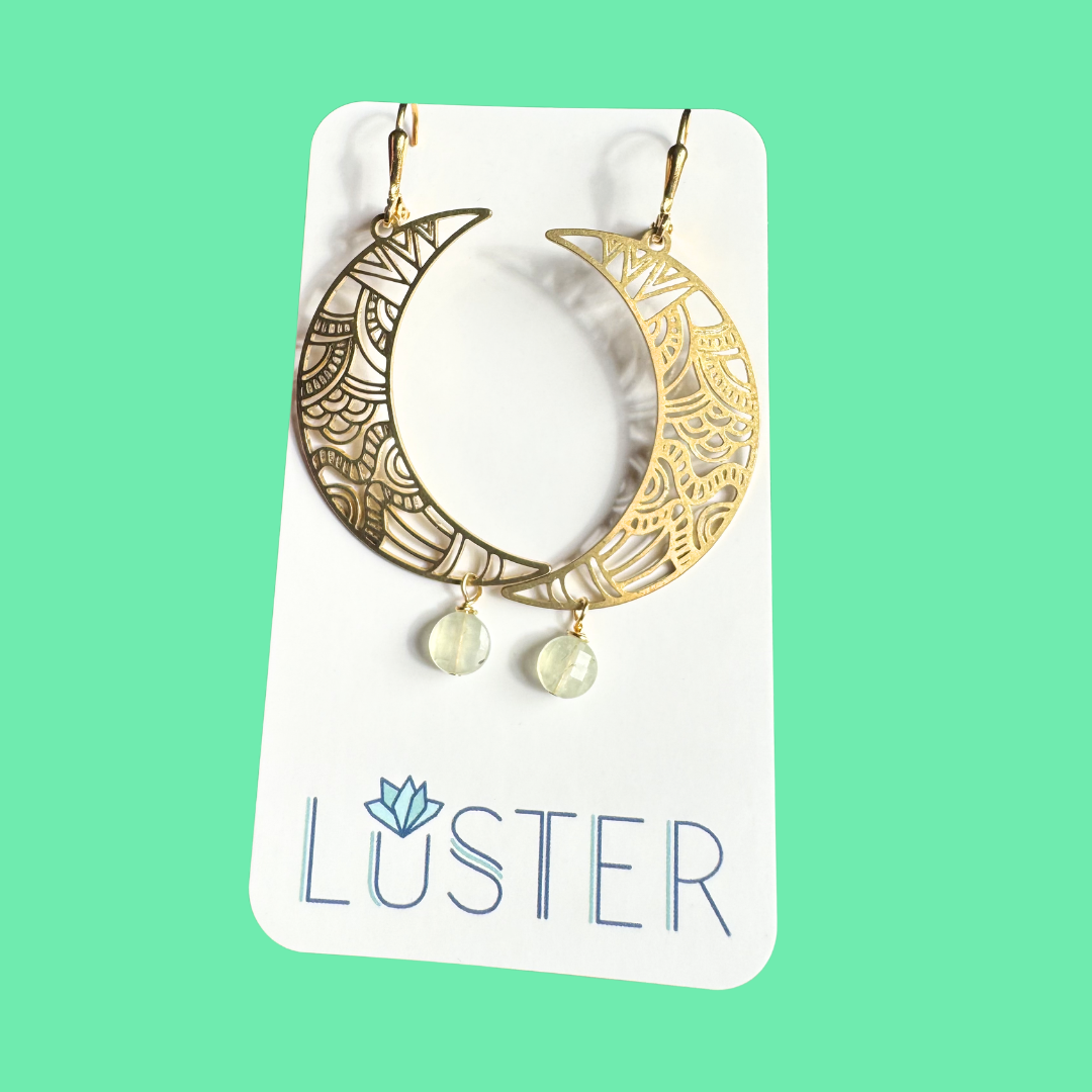 Gold hoop earrings with moon design on a Luster branded card against a green background