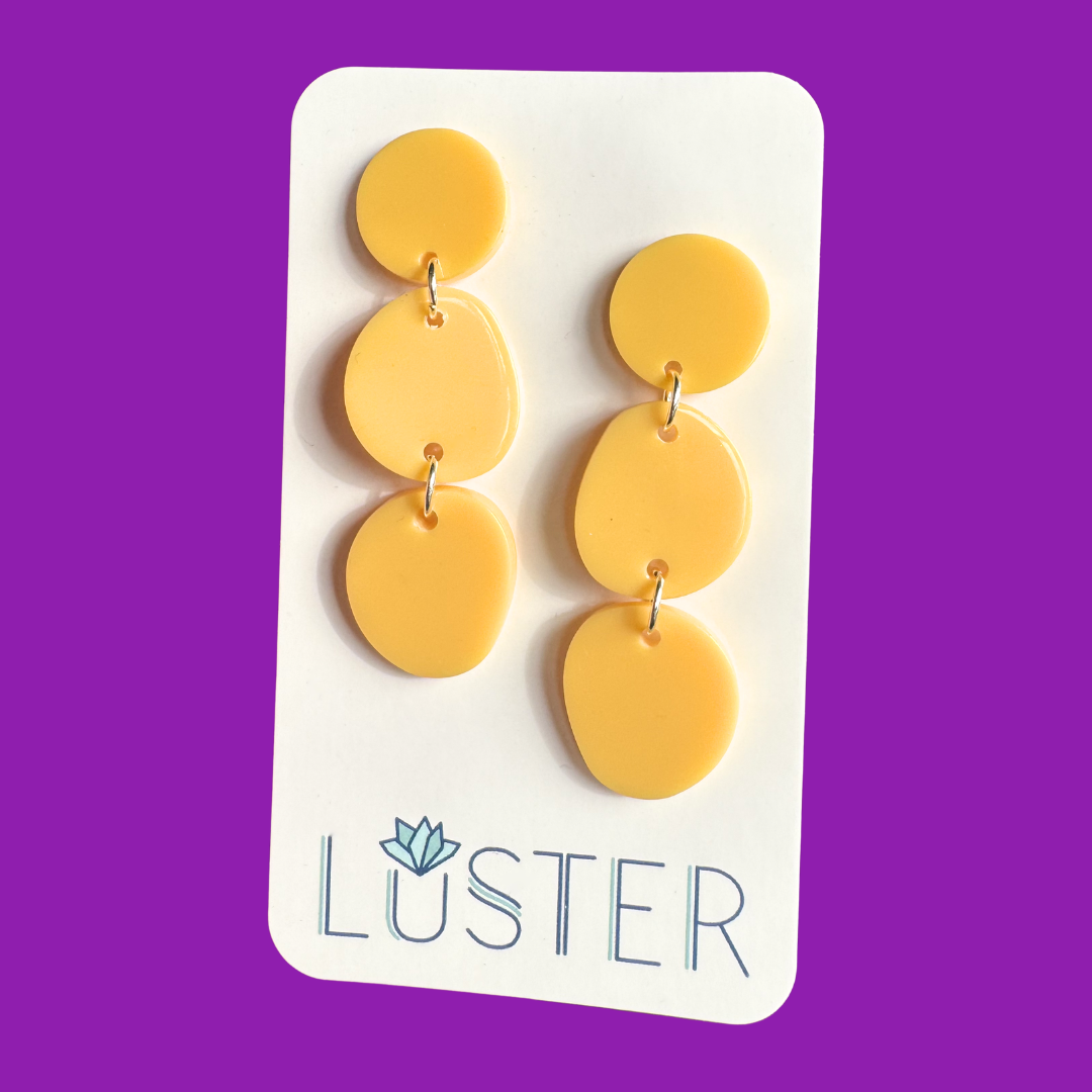 Yellow earrings on a Luster branded card against a purple background